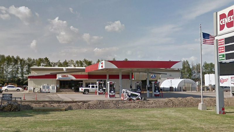 Cenex gas station with red and white canopy, multiple fuel pumps, convenience store building, and large roadside sign with U.S. flag nearby.