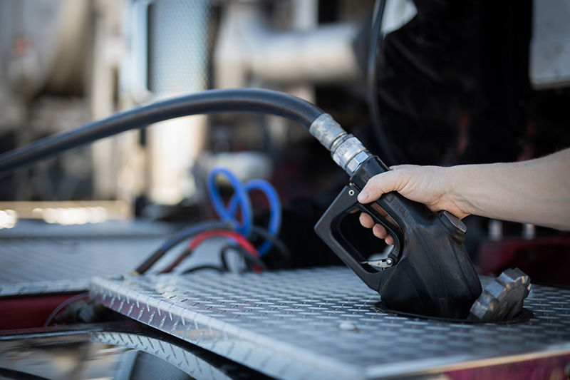 Close-up of a person refueling a large vehicle with a black fuel pump nozzle on a metal platform.